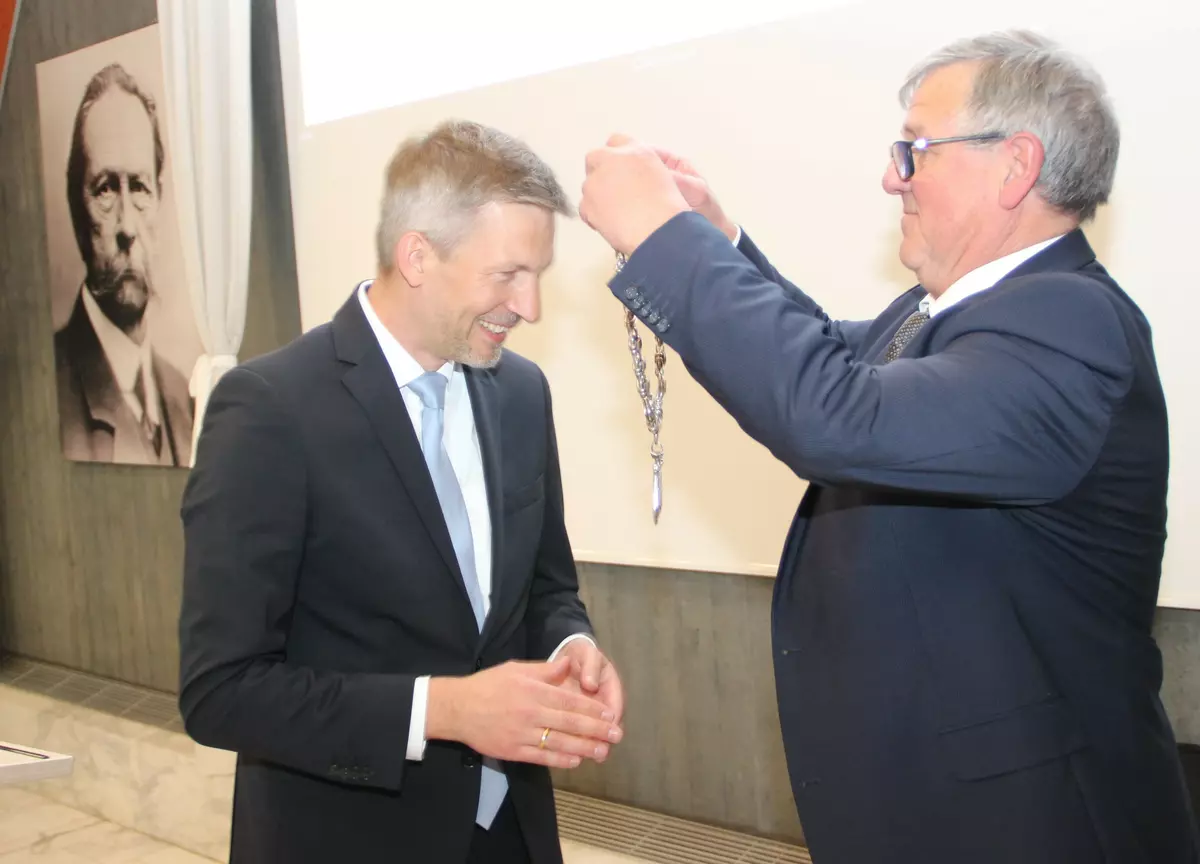 Der neugewählte (alte) Bürgermeister Schmutz erhält von seinem Stellvertreter Bläß die Amtskette umgelegt