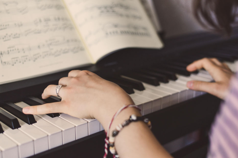 Hände spielen auf der Tastatur eines Klavier, ein Notenblatt davor