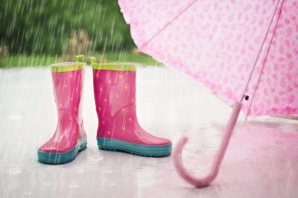 Rote Gummistiefel und rosa Schirm stehen auf dem Boden auf den es regnet